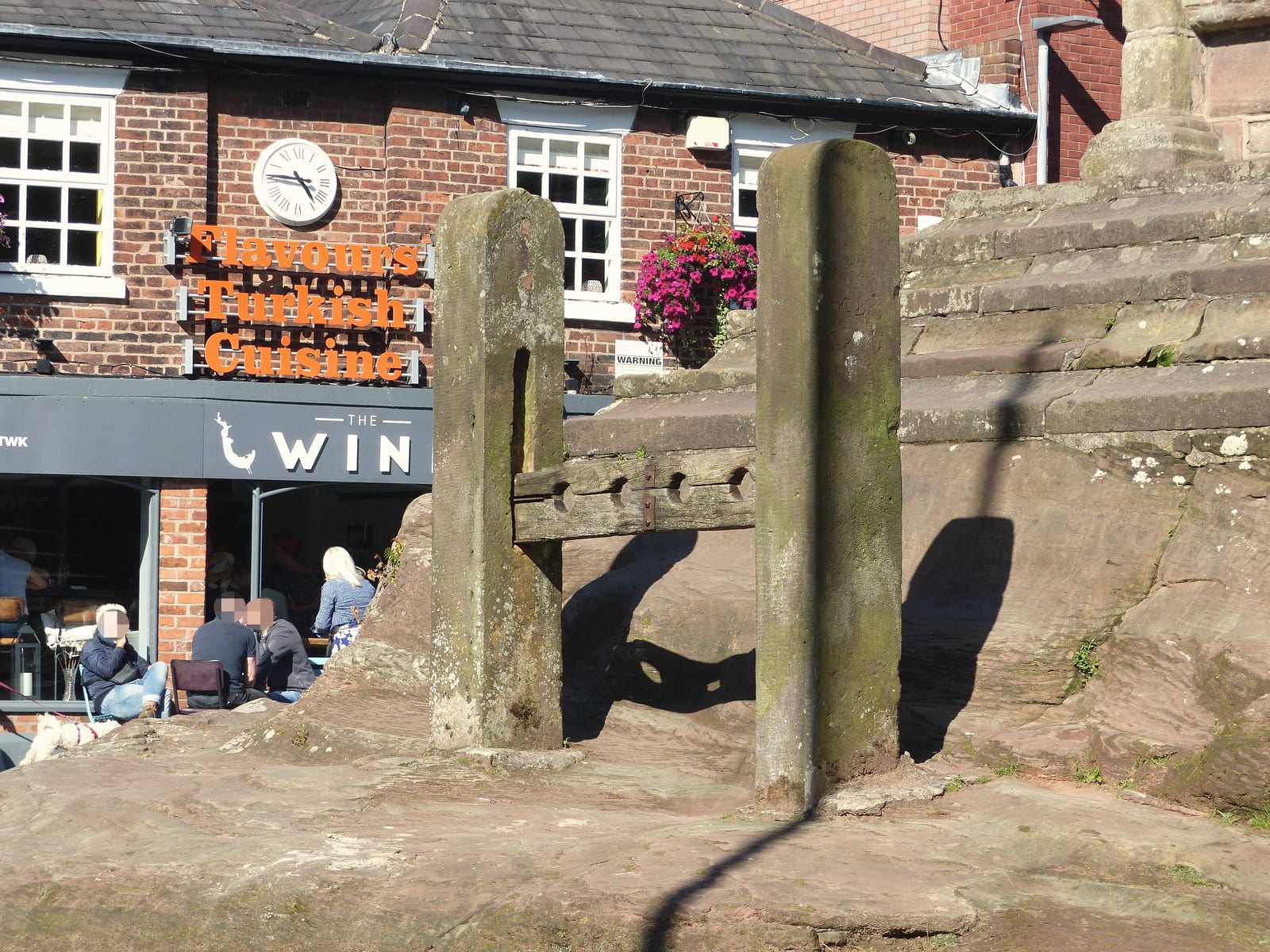 The old village stocks at Lymm Cross, with shops behind